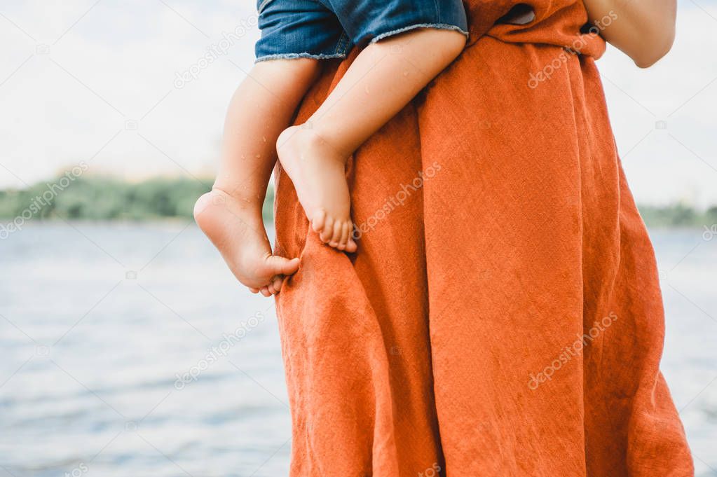 cropped image of mother in dress holding son near river