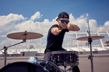 young tattooed drummer in sunglasses playing drums on street clipart