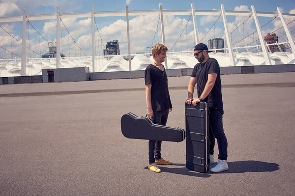 musicians with musical instruments in cases having conversation while standing on street