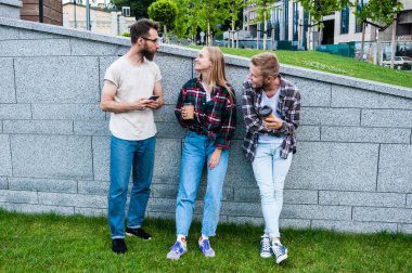 Smartphone kullanarak ve kağıt bardak kahve içme gülümseyen genç arkadaşlar