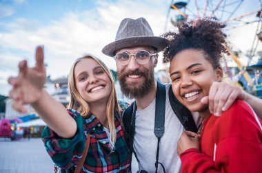 cheerful young multiethnic friends smiling at camera in amusement park clipart