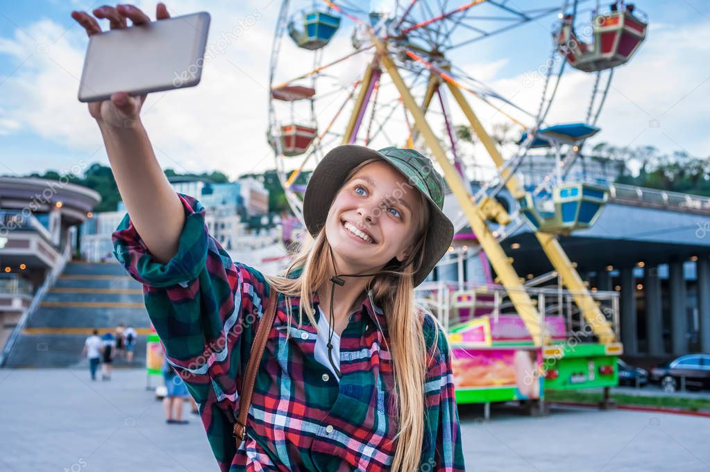 beautiful smiling blonde girl taking selfie with smartphone in amusement park