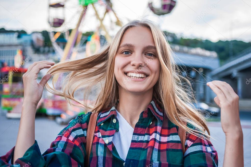 happy blonde girl smiling at camera while spending time in amusement park