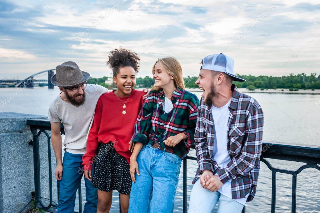 cheerful young multiethnic friends spending time together and laughing at riverside