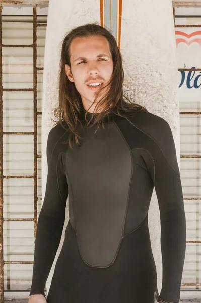 Портрет человека с длинными волосами в гидрокостюме с доской для серфинга, смотрящего в сторону — стоковое фото