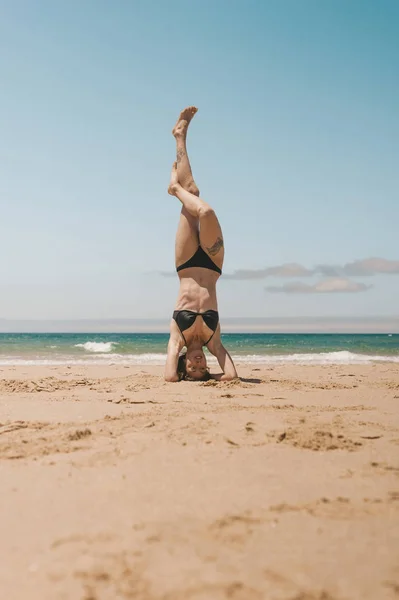 Young woman practicing headstand on sandy beach on summer day — Stock Photo