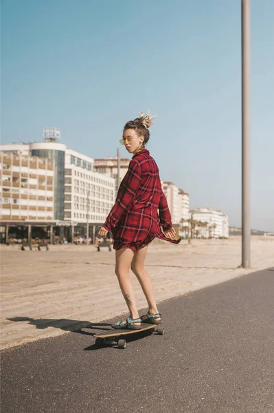 Mujer joven en gafas de sol y camiseta patinaje en longboard en la calle en Portugal - foto de stock