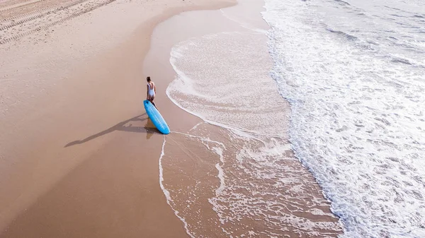 Vista aérea de mujer joven en traje de baño tirando de la tabla de surf en la playa de arena, Ashdod, Israel - foto de stock