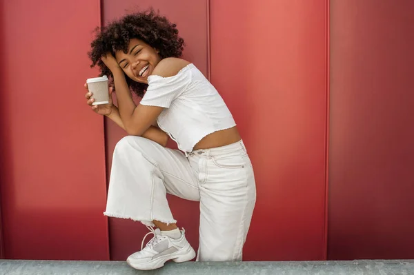 Glücklich afrikanisch-amerikanisches Mädchen hält Einweg-Kaffeetasse und lacht auf der Straße — Stockfoto