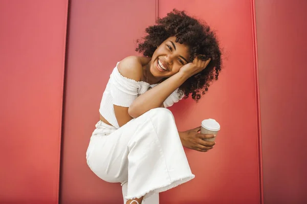 Hermosa chica afroamericana feliz sosteniendo taza de papel y sonriendo a la cámara - foto de stock