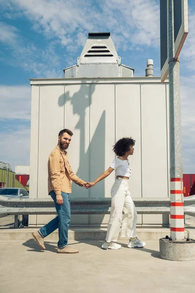 Feliz elegante jovem casal multiétnico de mãos dadas e caminhando juntos na rua — Fotografia de Stock