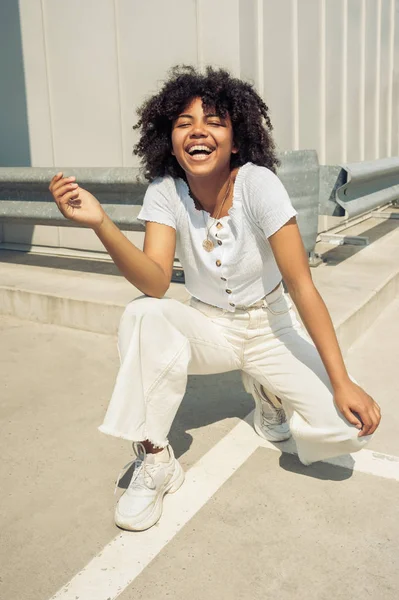 Heureuse jeune femme afro-américaine accroupie et riant dans la rue — Photo de stock