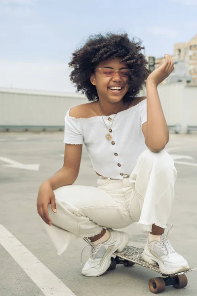 Happy young african american woman crouching on skateboard and laughing on street — Stock Photo