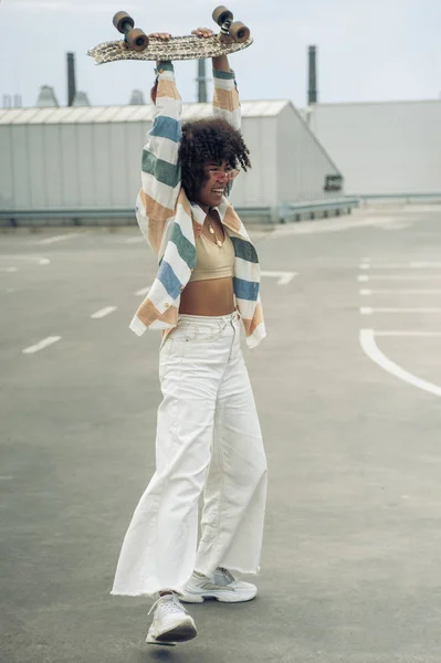 Joyeuse jeune femme afro-américaine tenant skateboard dans la rue — Photo de stock