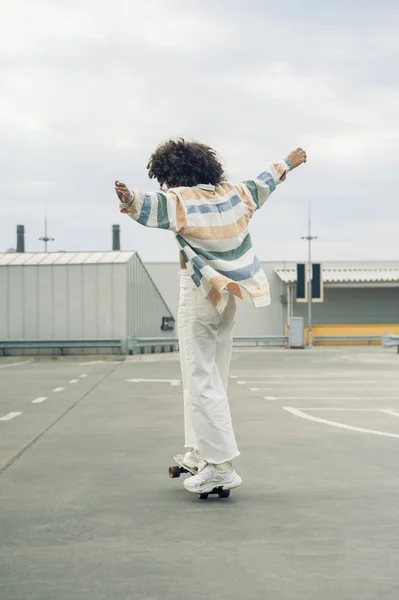 Back view of young woman with open arms skateboarding on street — Stock Photo