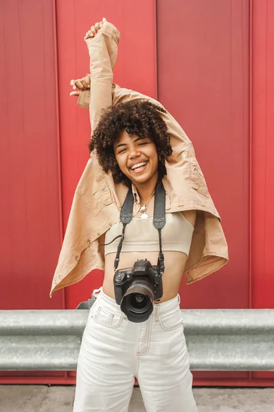 Cheerful african american girl with camera raising hands on street — Stock Photo