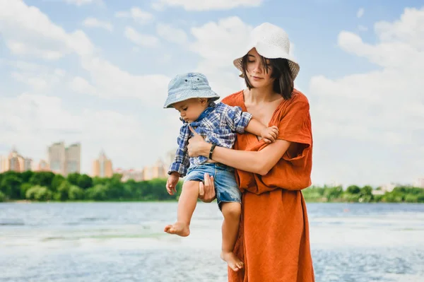 Mãe segurando filho perto do rio no verão — Fotografia de Stock