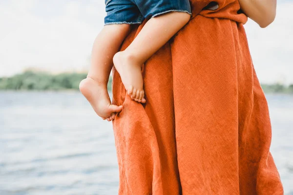 Imagen recortada de la madre en vestido sosteniendo hijo cerca del río - foto de stock