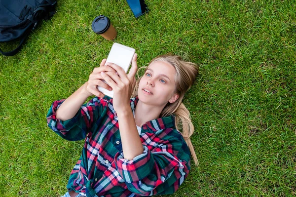 Vue du haut de la jeune femme blonde allongée sur l'herbe et utilisant un smartphone — Photo de stock