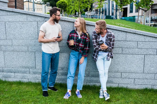 Smiling young friends using smartphone and drinking coffee from paper cups — Stock Photo