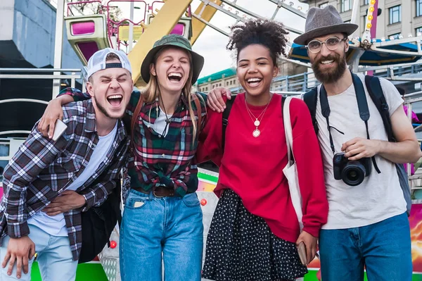 Felices jóvenes amigos multiétnicos de pie juntos y riendo en el parque de atracciones - foto de stock