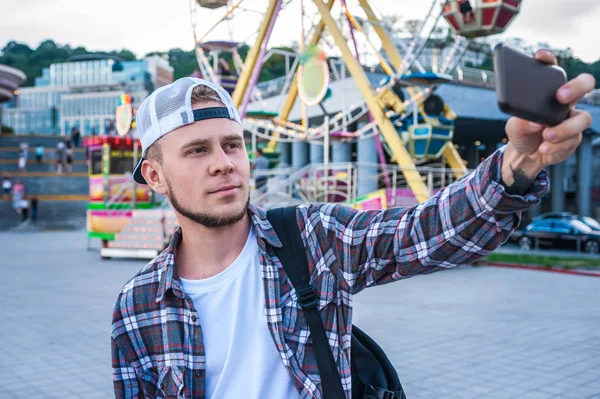 Handsome young man taking selfie with smartphone in amusement park — Stock Photo