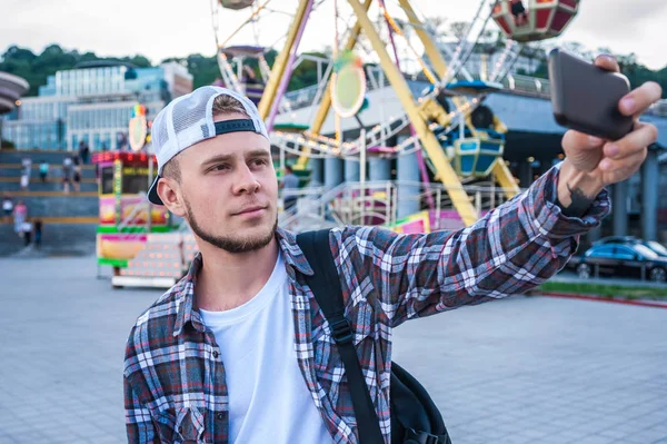 Beau jeune homme prenant selfie avec smartphone dans le parc d'attractions — Photo de stock