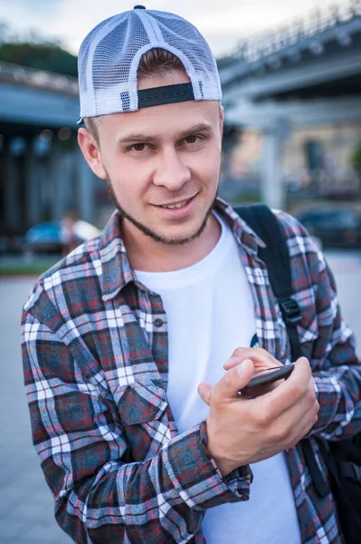 Joven guapo usando teléfono inteligente y sonriendo a la cámara - foto de stock