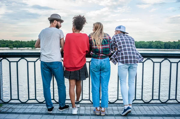 Vue arrière de quatre jeunes amis multiethniques debout ensemble sur un remblai — Photo de stock
