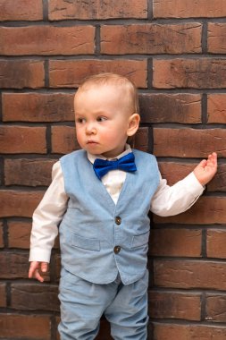 Mavi elbiseli küçük bir çocuk ve lekeli mavi bir kelebek bir kahverengi tuğla duvara yakın duruyor