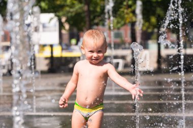 Küçük çocuk bir jeti su sokak Çeşmesi ile oynarken bir sıcak yaz gününde gülümseyen