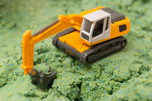 Toy excavator on tracks digging a hole in the green and yellow sand
