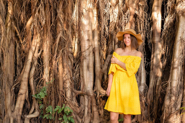 Girl in a yellow dress and hat against the backdrop of tropical wood