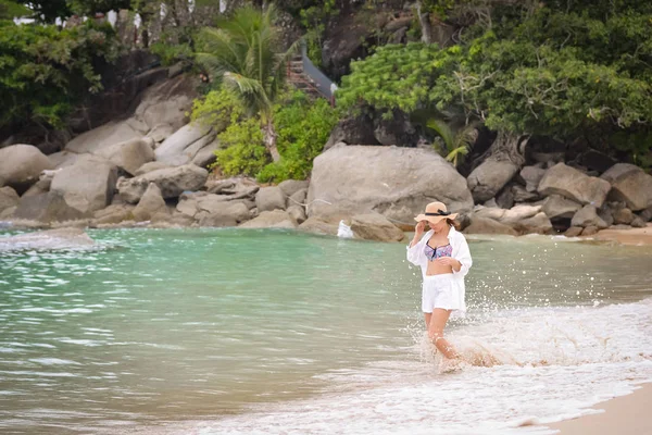 Chica de camisa blanca y sombrero caminando por la playa — Foto de Stock