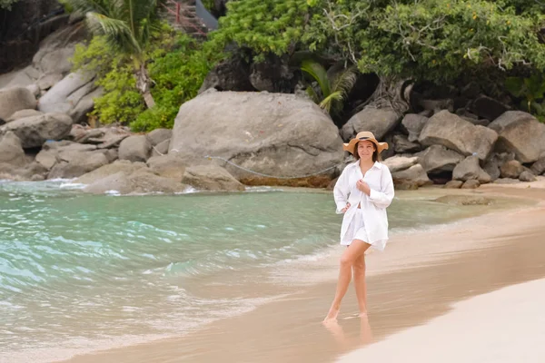 Chica de camisa blanca y sombrero caminando por la playa — Foto de Stock