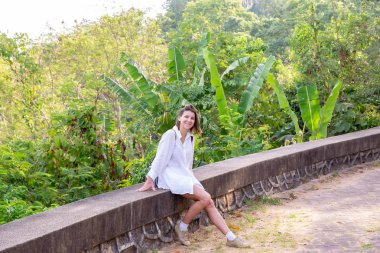 Beyaz bir gömlek tropikal ağaçlar bir arka plan üzerinde oturan kız