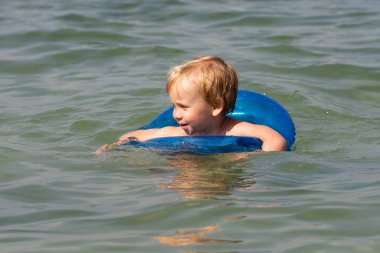 Küçük çocuk mavi bir şişme daire ile denizde yüzme