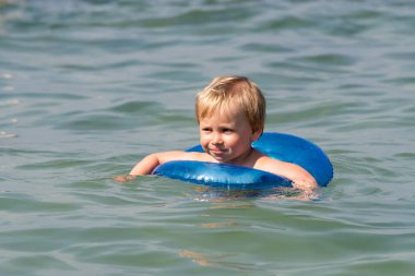 Küçük çocuk mavi bir şişme daire ile denizde yüzme