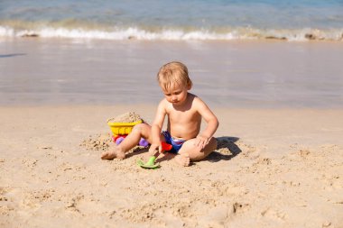 Küçük çocuk bir kürek ve bir araba ile deniz kenarında kum üzerinde oynuyor