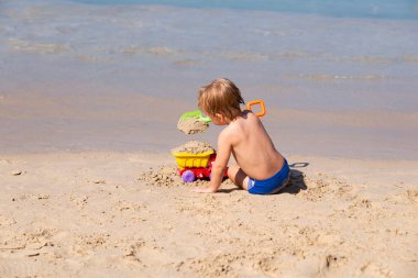 Küçük çocuk bir kürek ve bir araba ile deniz kenarında kum üzerinde oynuyor