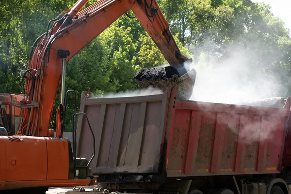 Scarico di asfalto grezzo caldo dal camion con l'aiuto di un escavatore — Foto Stock