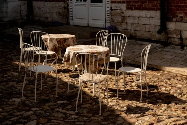 Metal restaurant furniture on cobblestone street in the sun