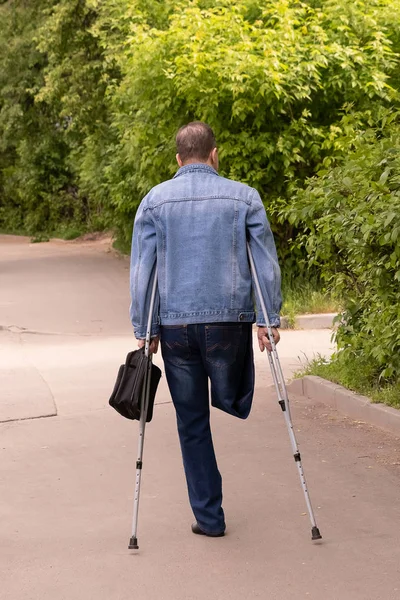 Pessoa com deficiência sem perna direita está em muletas na cidade, uma vista a partir das costas . — Fotografia de Stock