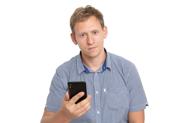 Дневной портрет молодого европейского кавказца на белом фоне в синей рубашке, стоящей перед камерой, с телефоном в руке и улыбающейся — стоковое фото