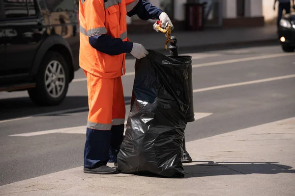 The janitor takes the trash out of the street urn and puts it in a big black bag — Stock Photo, Image