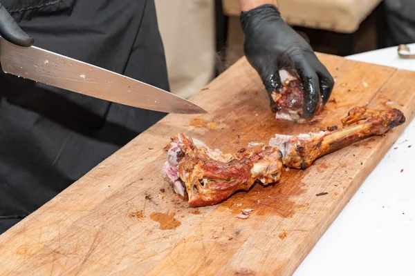 Kuchař v černé rukavice dělené šťavnaté maso steak na dřevěné desce s nožem, detail. Lahodné, šťavnaté, čerstvě vařené maso steaky vařit maso na prkénku. — Stock fotografie