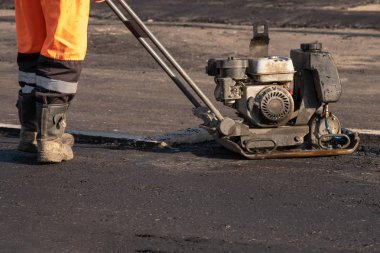 Yol işçileri yolda titreşimli bir Rammer ile asfalt kompakt. Bir yol inşaatı yerinde kompaktör ile çalışan