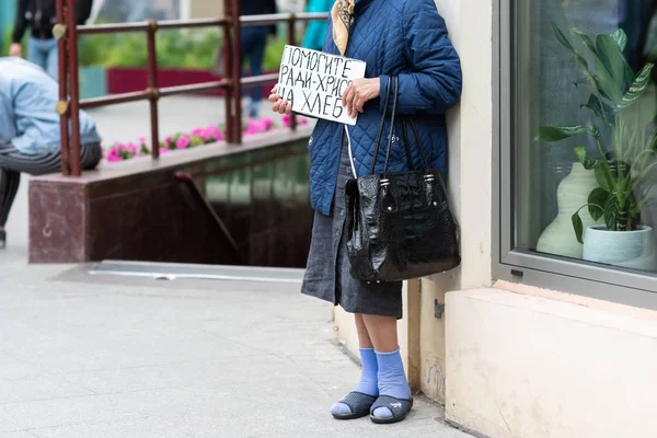Elinde karton olan yaşlı bir kadın sokakta para ister. Yazıt "Ekmek üzerinde İsa aşkına yardım" — Stok fotoğraf