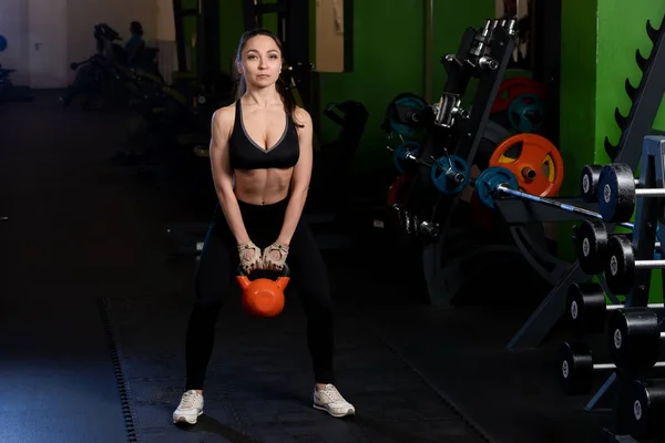 Joven mujer fitness balanceando el kettlebell durante el entrenamiento crossfit. Chica atlética haciendo ejercicio en un gimnasio . — Foto de Stock