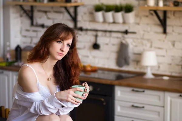 Sevimli güzel sevimli neşeli güzel trendy şık kız kahve içme, modern ışık beyaz mutfakta masa tezgahında oturan — Stok fotoğraf